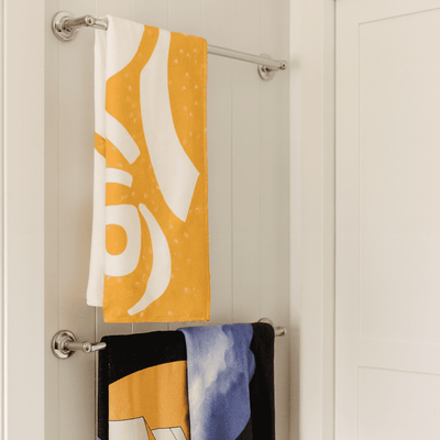 Bath Towel - A yellow bath towel with a pattern hangs above a black towel featuring a design, both on a towel rack.