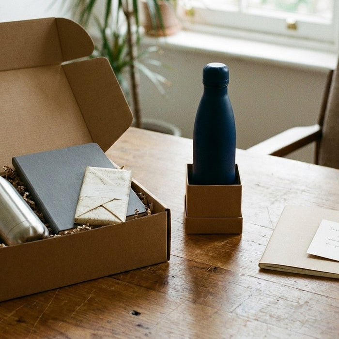Three tiers of client gifts on a desk: a curated gift box, a boxed insulated bottle and a notebook with a handwritten card