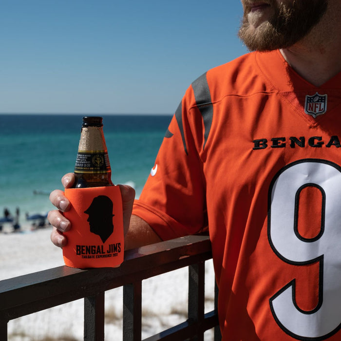 Man in Bengals jersey enjoying beer by the beach on a sunny day.