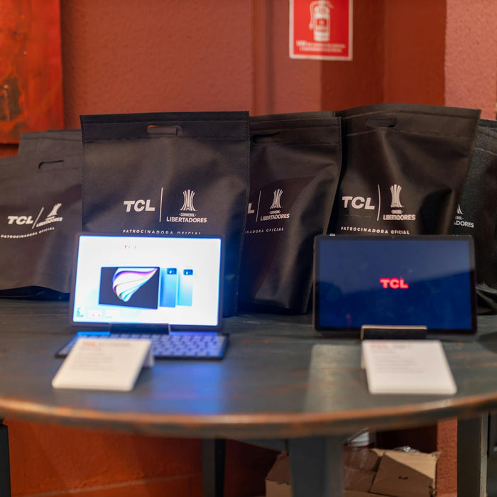 A promotional setup showcasing TCL tablets and branded gift bags on a round table indoors.