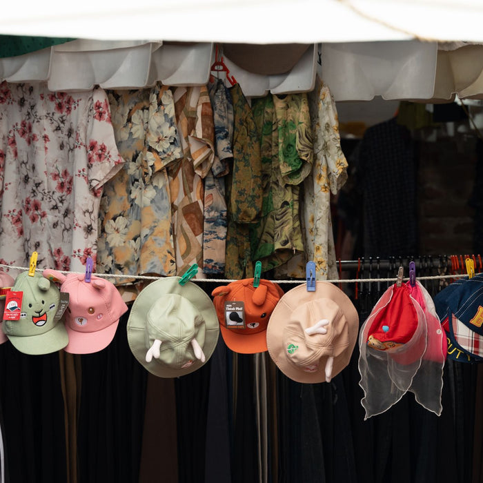 Vibrant display of hats and floral dresses at outdoor market, perfect for festivals.