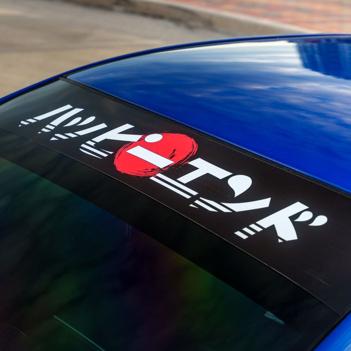 Close-up of a car's windshield with a Japanese-themed decal on a sunny day.