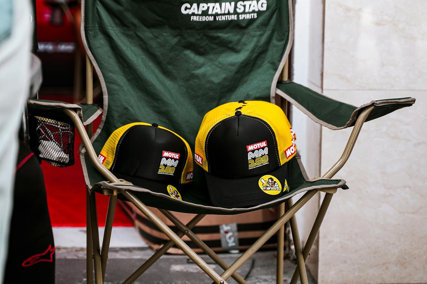 Black and yellow caps with Motul branding on a green foldable chair indoors.