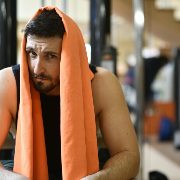A tired man rests with an orange towel after a workout in the gym.