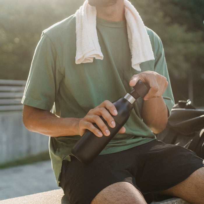 Close-up of a man sitting outdoors with a reusable water bottle and towel.