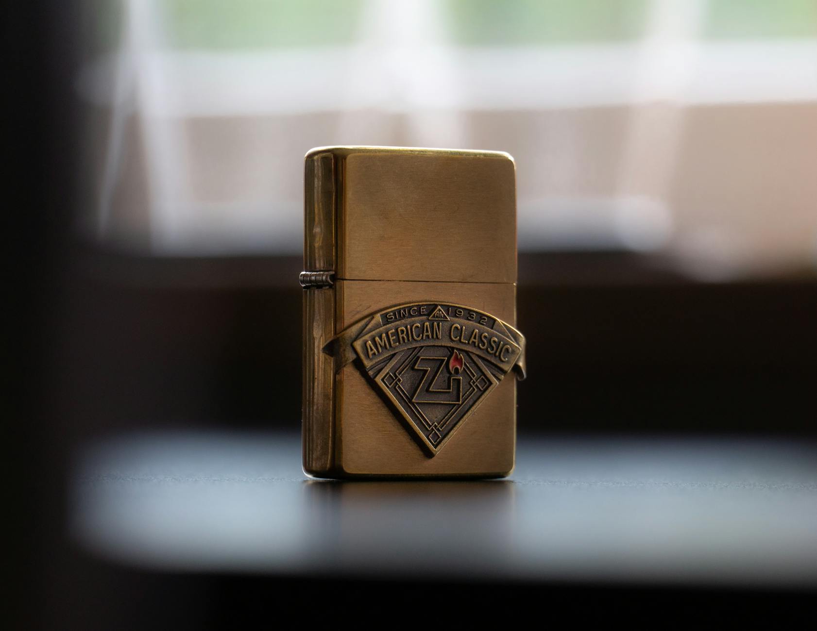Close-up of a vintage brass Zippo lighter with American Classic logo, captured in soft lighting.