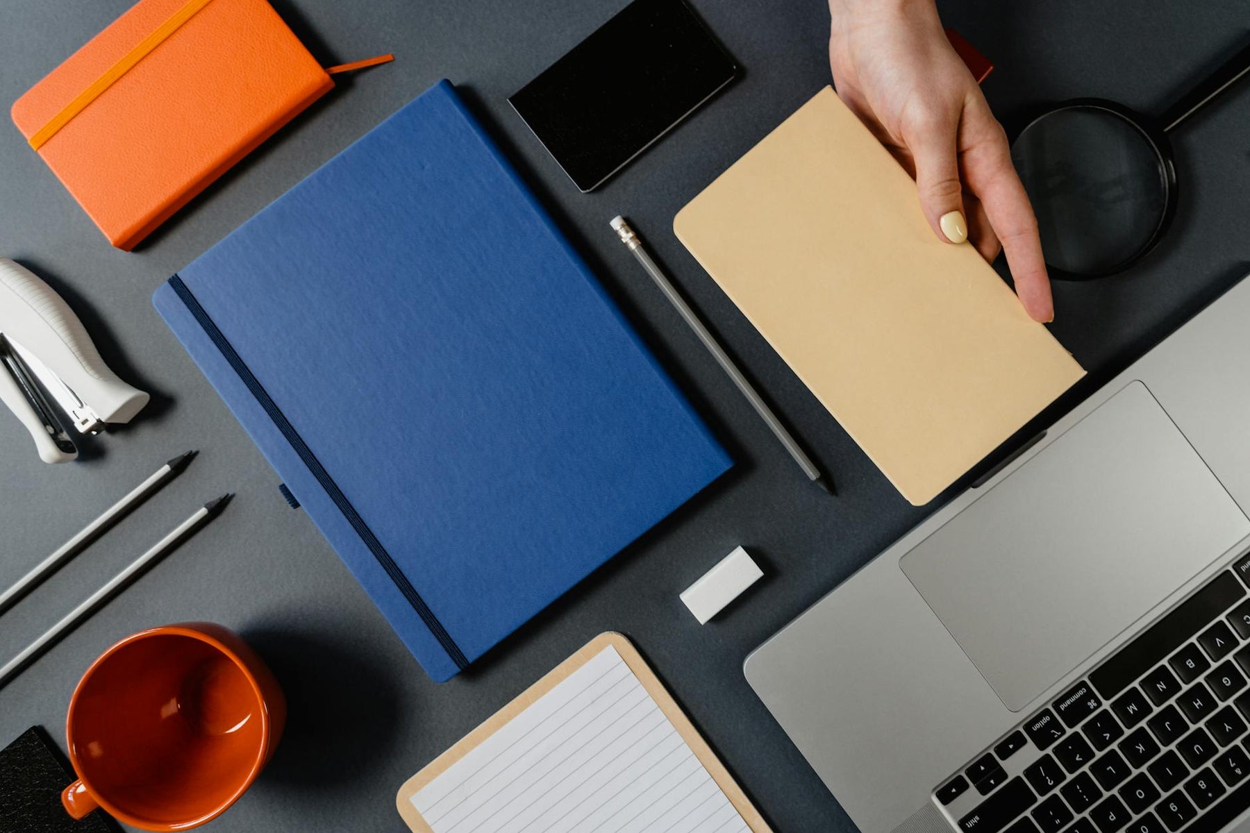 Organized desk layout from above featuring notebooks, laptop, and office supplies.