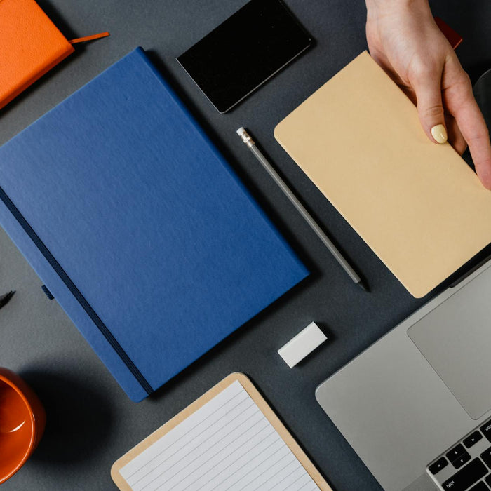 Organized desk layout from above featuring notebooks, laptop, and office supplies.