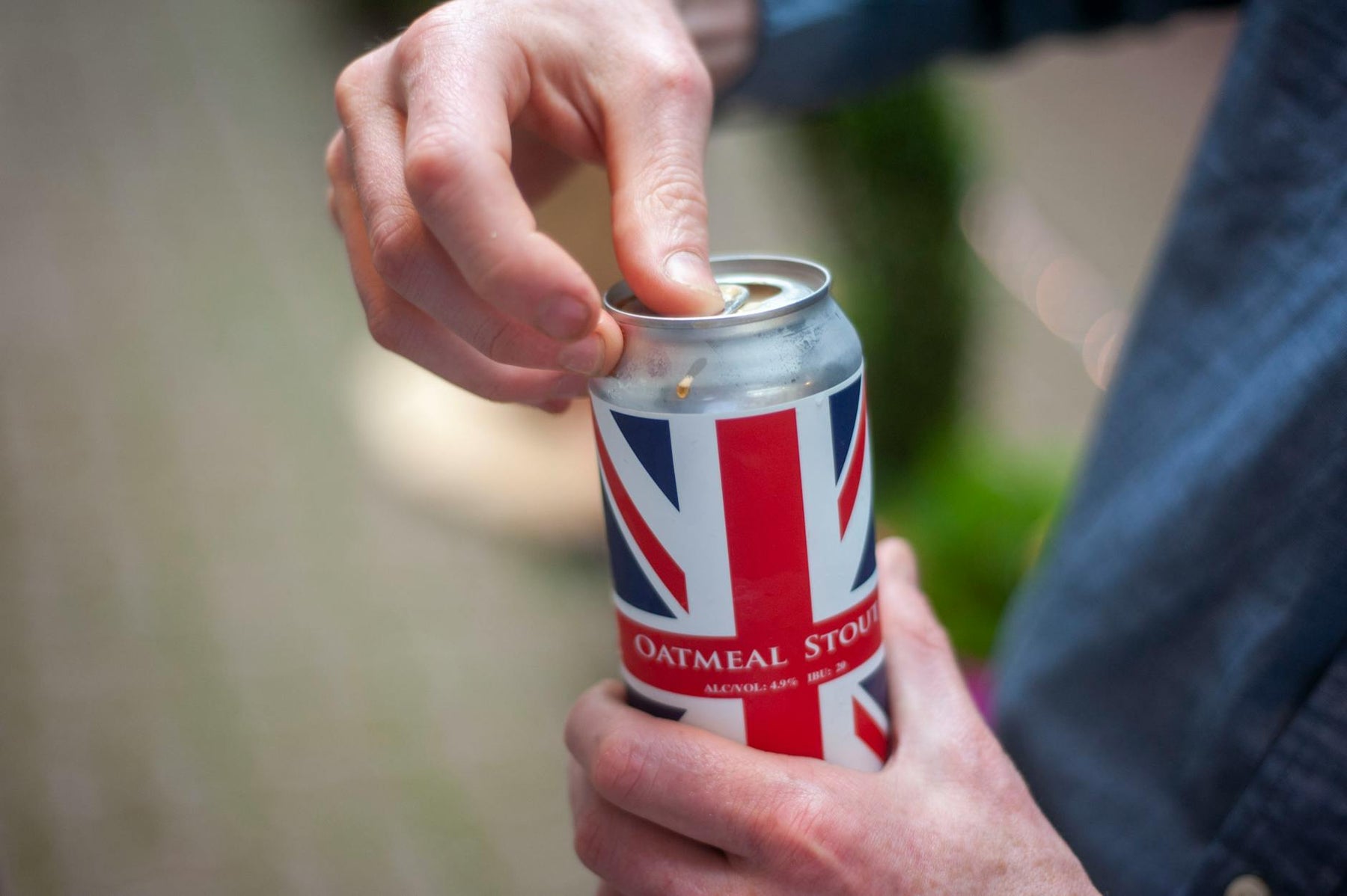 Close-up of a person opening a can of oatmeal stout beer with a Union Jack design outdoors.