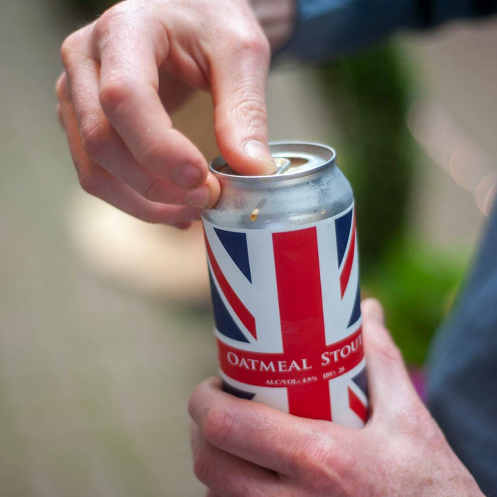Close-up of a person opening a can of oatmeal stout beer with a Union Jack design outdoors.