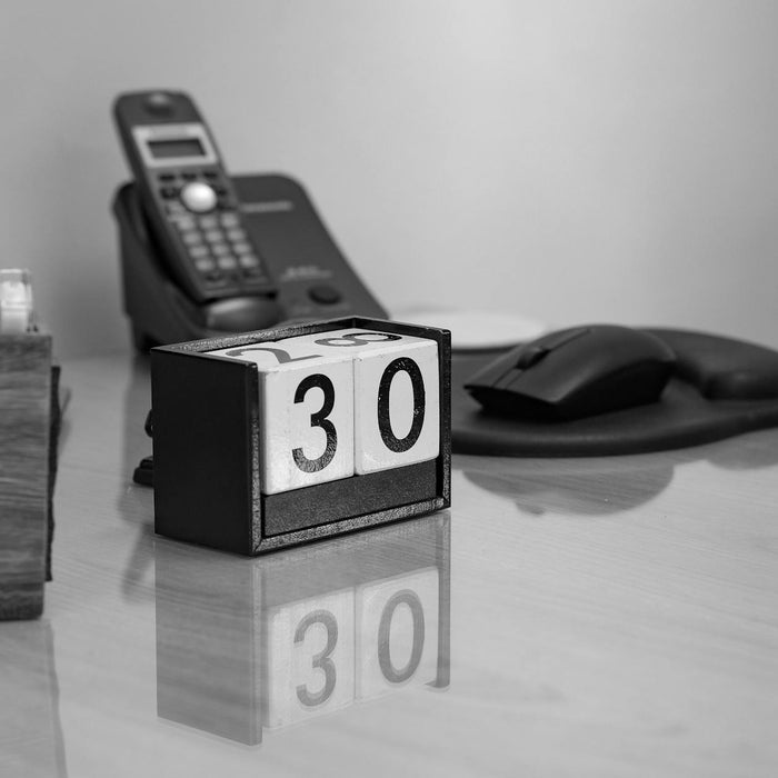 Monochrome image of an office desk with a perpetual calendar, phone, and monitor.