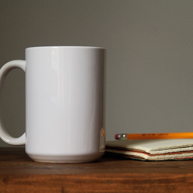 white ceramic mug beside orange pencil on open book page