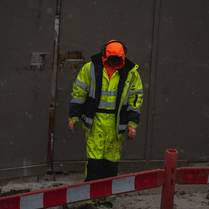 man in green jacket and orange helmet standing on gray concrete floor