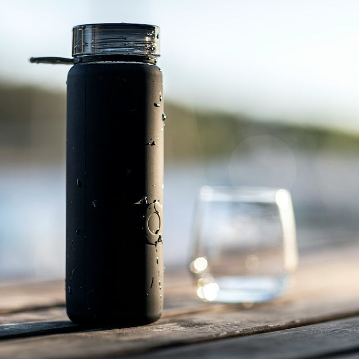 black bottle beside clear drinking glass on brown wooden table