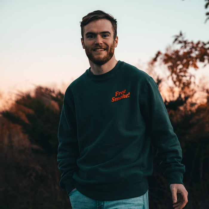a man in a green sweatshirt standing in front of trees