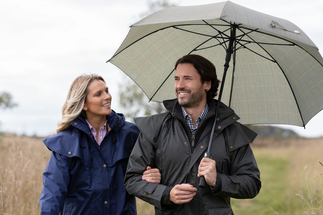 a man and a woman walking in a field holding an umbrella