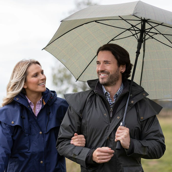 a man and a woman walking in a field holding an umbrella