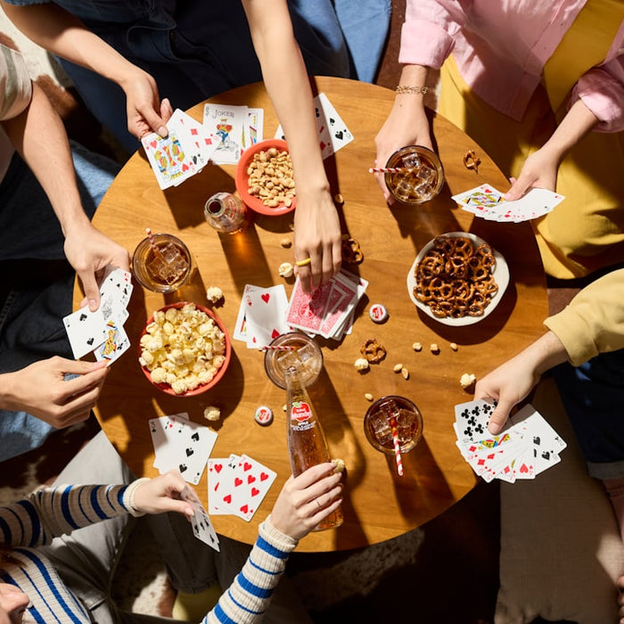 Friends play cards, sharing snacks and drinks.