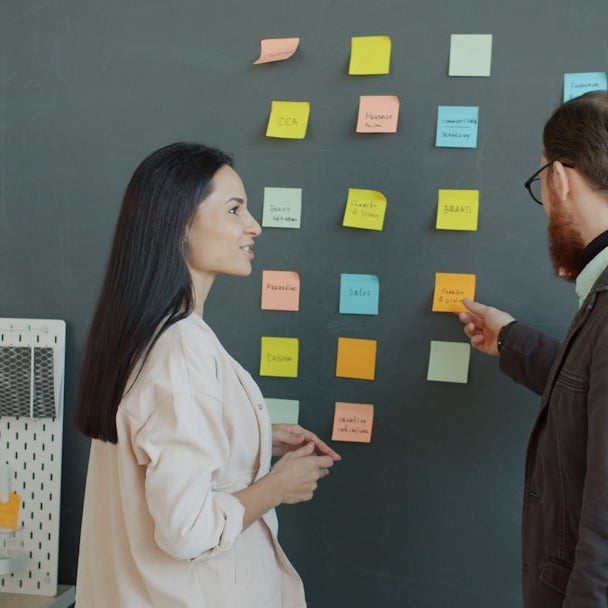 Two colleagues discussing sticky notes on a wall.