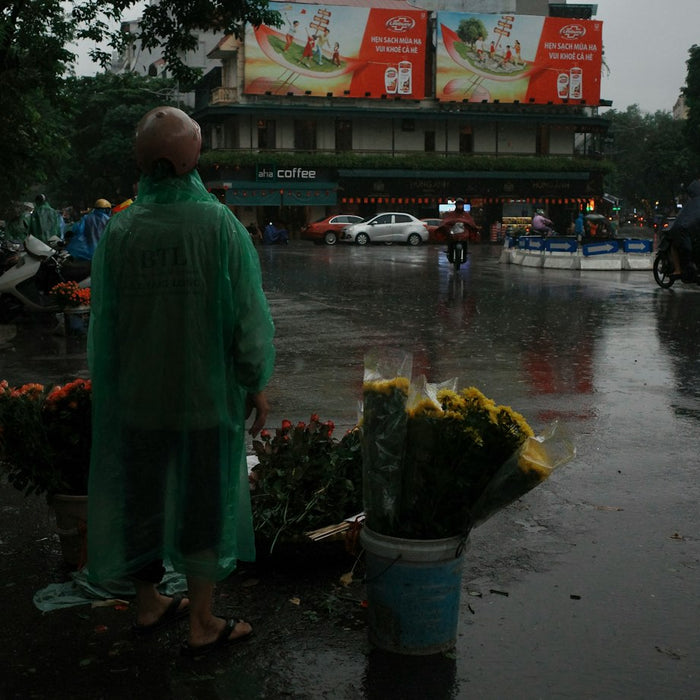 Person in green raincoat stands by flower stall in rain