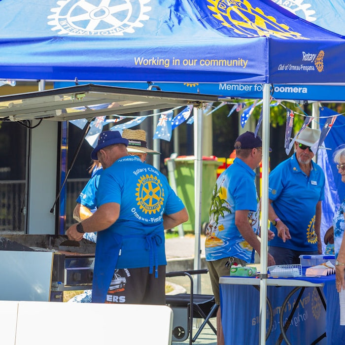People gathered under blue rotary tents at an outdoor event.