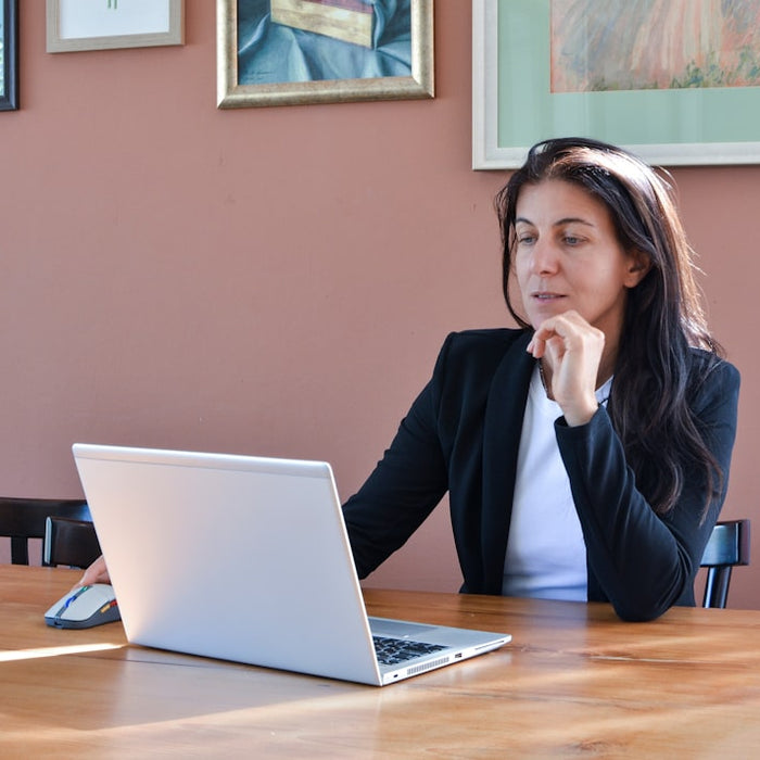 Woman in a black blazer working on a laptop.