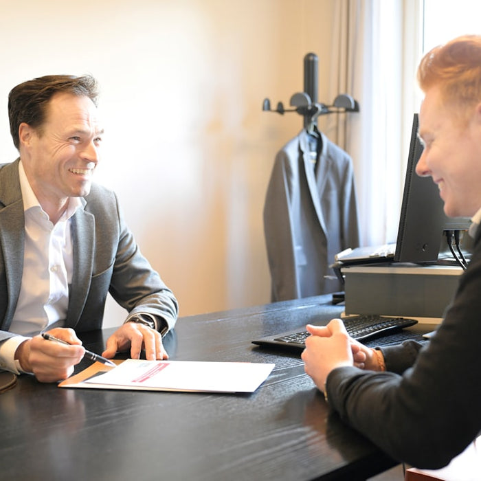 Two smiling men discussing documents at an office desk.