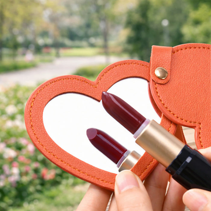 Heart-Shaped Compact Mirror with Keychain - A heart-shaped compact mirror with an orange exterior, featuring a reflective surface and two lipstick shades beside it.