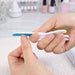 Foldable Nail File Block - A foldable nail file block in white and blue, held between fingers, with blurred nail polish bottles in the background.