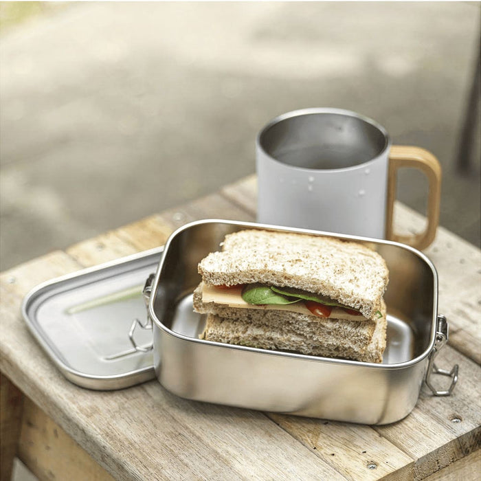 Seasons Titan Recycled Stainless Steel Lunch Box - A stainless steel lunch box with a sandwich inside, placed beside a drink bottle on a wooden surface.