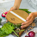 NATURA Iris Glass Food Container - A glass food container with a bamboo lid, surrounded by fresh vegetables like spinach and radishes.