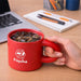 Laser Engraving Ceramic Coffee Mug - A red ceramic coffee mug being held, filled with iced drink, alongside a laptop and stationery items on a desk.