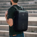 Bobby Bizz Anti-theft Backpack  Briefcase - A black anti-theft backpack with a sleek design, featuring a logo and a top handle, worn on a person’s back.