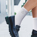 June Crew Socks - White crew socks with ribbed texture, worn with black loafers, featuring a logo. Suitable for casual or stylish outfits.