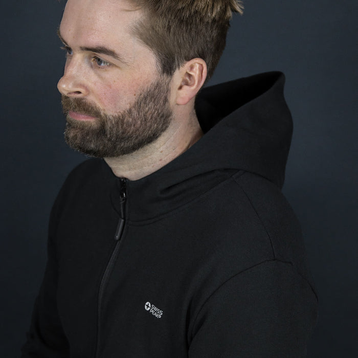Swiss Peak Urban Hoodie - A black hoodie with a zip and a logo, worn by a man with short hair and a beard against a dark background.
