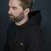 Swiss Peak Urban Hoodie - A black hoodie with a zip and a logo, worn by a man with short hair and a beard against a dark background.