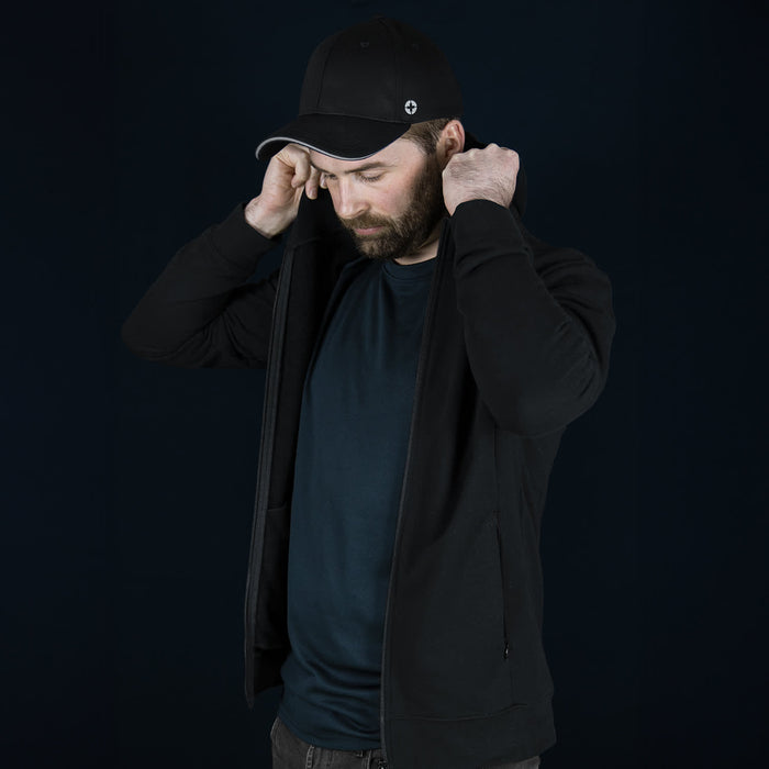 Swiss Peak Urban Hoodie - A man in a black Swiss Peak Urban Hoodie adjusts the hood, wearing a black cap. The background is dark.
