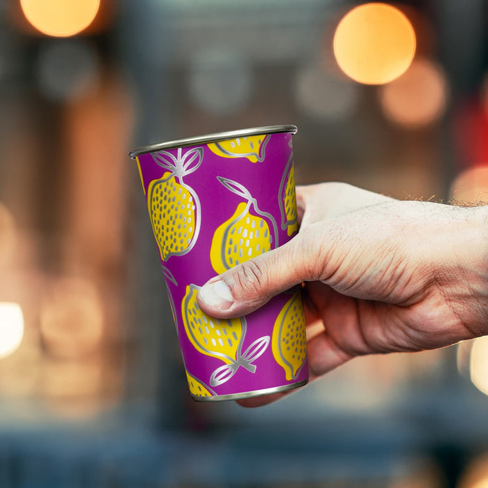 Burano Colour Changing Cup - A drink cup featuring a vibrant purple design with yellow lemons and a silver rim, held in a hand.