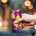 Burano Colour Changing Cup - A drink cup featuring a vibrant purple design with yellow lemons and a silver rim, held in a hand.