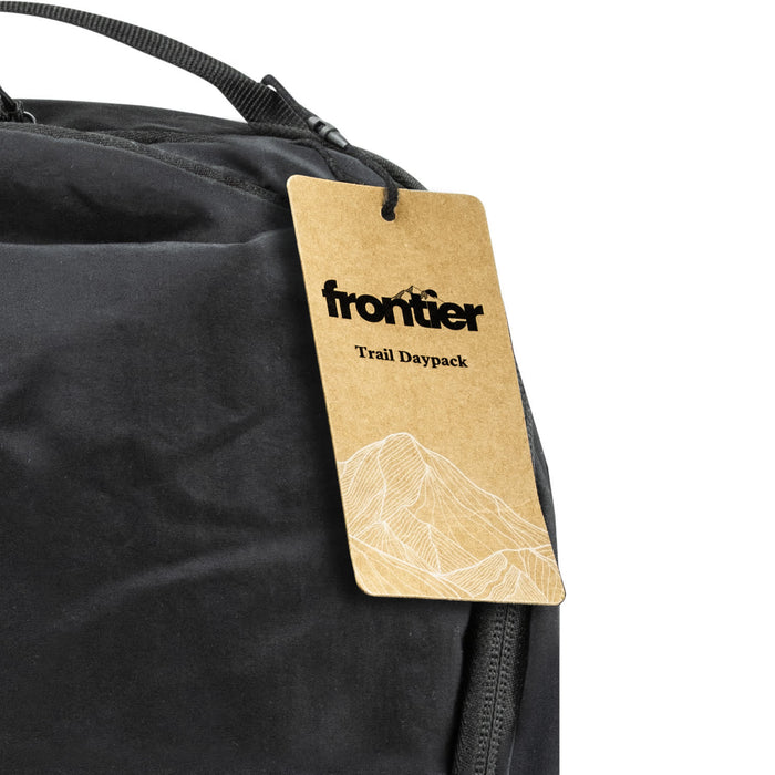 Frontier Trail Daypack - A black daypack with a tag attached, featuring a simple mountain graphic and a logo.