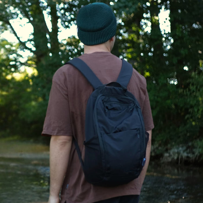 Frontier Trail Daypack - A black daypack worn on the back of a person in a forested setting, with green foliage in the background.