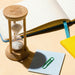 Tempus Bamboo Hourglass - A bamboo hourglass with sand sits beside a notebook, a yellow notepad, and a blue sticky note with a paperclip.
