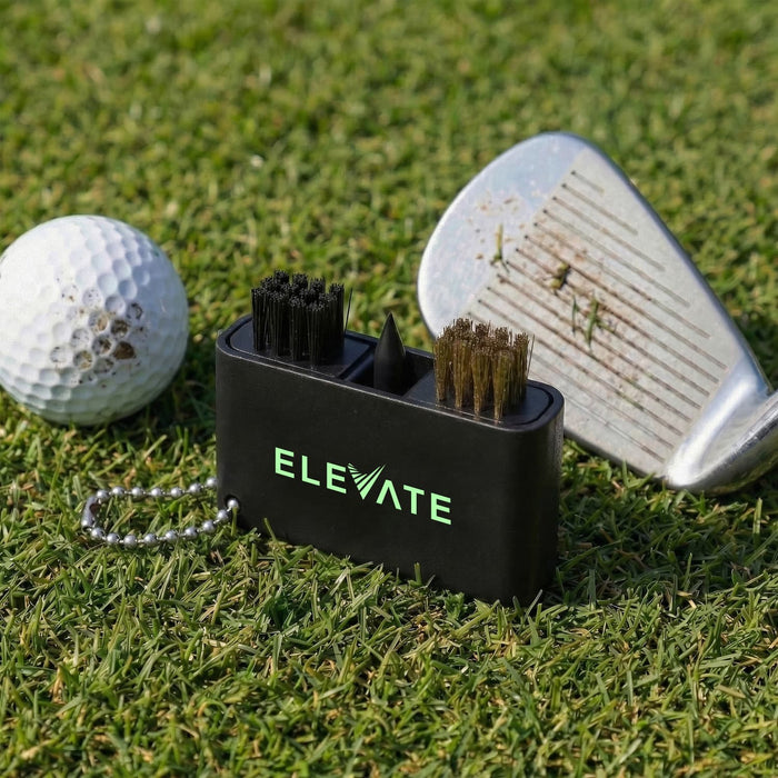Caddie Golf Club Cleaning Tool - A black golf club cleaning tool with brushes sits on grass next to a golf ball and a club with dirt on it.