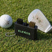 Caddie Golf Club Cleaning Tool - A black golf club cleaning tool with brushes sits on grass next to a golf ball and a club with dirt on it.