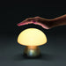 Portobello Table Lamp - A mushroom-shaped table lamp with a white dome and a metallic base, with a hand positioned above it.