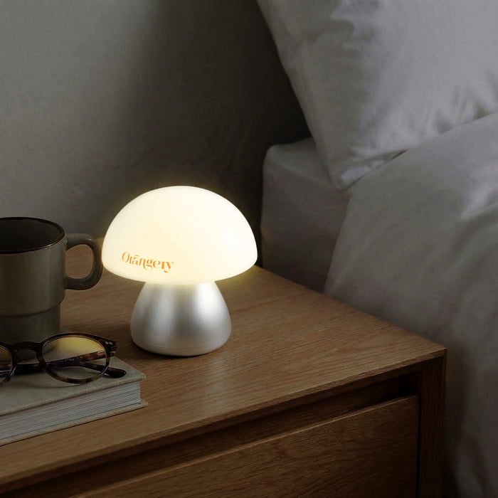 Portobello Table Lamp - A table lamp with a soft, white dome shade and a silver base, placed on a wooden bedside table with a coffee cup and glasses.
