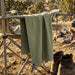Frontier Rapid Dry Towel - A green Frontier Rapid Dry Towel hangs from a camping chair beside a fire, with boots on the ground nearby.