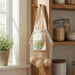 Cotton Mesh Foldaway Tote Bag - Small - A small, cream-coloured cotton mesh tote bag hangs on a hook, holding a few onions. It features a logo on the front.
