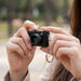 Candid Mini Camera - A compact black camera held in a person's hand, featuring a keychain attachment.