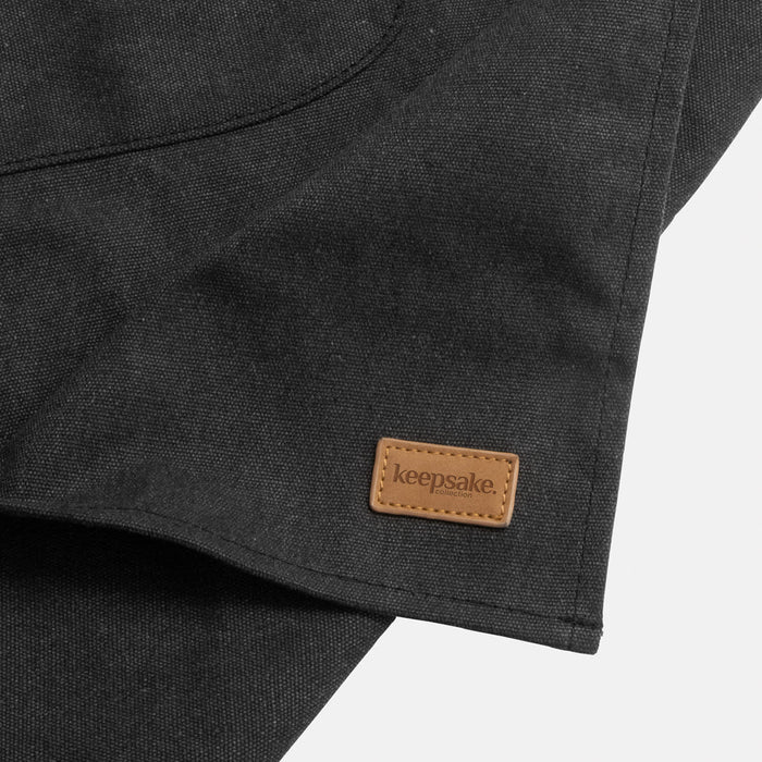 Keepsake Canvas Apron & Oven Mit Set - A dark grey canvas apron featuring a small leather logo tag, neatly folded to reveal texture and design.